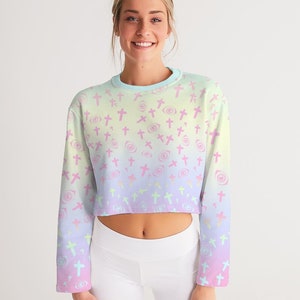 May include: A pastel rainbow ombre cropped sweatshirt with a pattern of pink crosses and swirls. The sweatshirt has long sleeves and a crew neck.