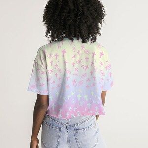 May include: A pastel pink, yellow and blue ombre cropped t-shirt with a pattern of pink crosses and white eyes.