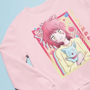 May include: Pink sweatshirt with a graphic of a girl with pink hair and cat ears holding a blue cat. The graphic is in a colorful frame with stars and the text "好きじゃない" in Japanese.