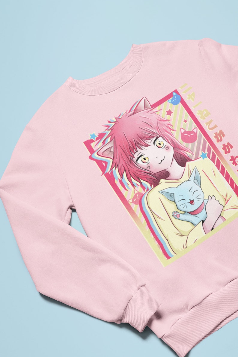 May include: Pink sweatshirt with a graphic of a girl with pink hair and cat ears holding a blue cat. The graphic is in a colorful frame with stars and the text "好きじゃない" in Japanese.