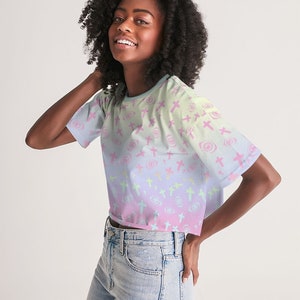 May include: A pastel pink, blue and green cropped t-shirt with a repeating pattern of crosses and swirls. The shirt has short sleeves and a relaxed fit.