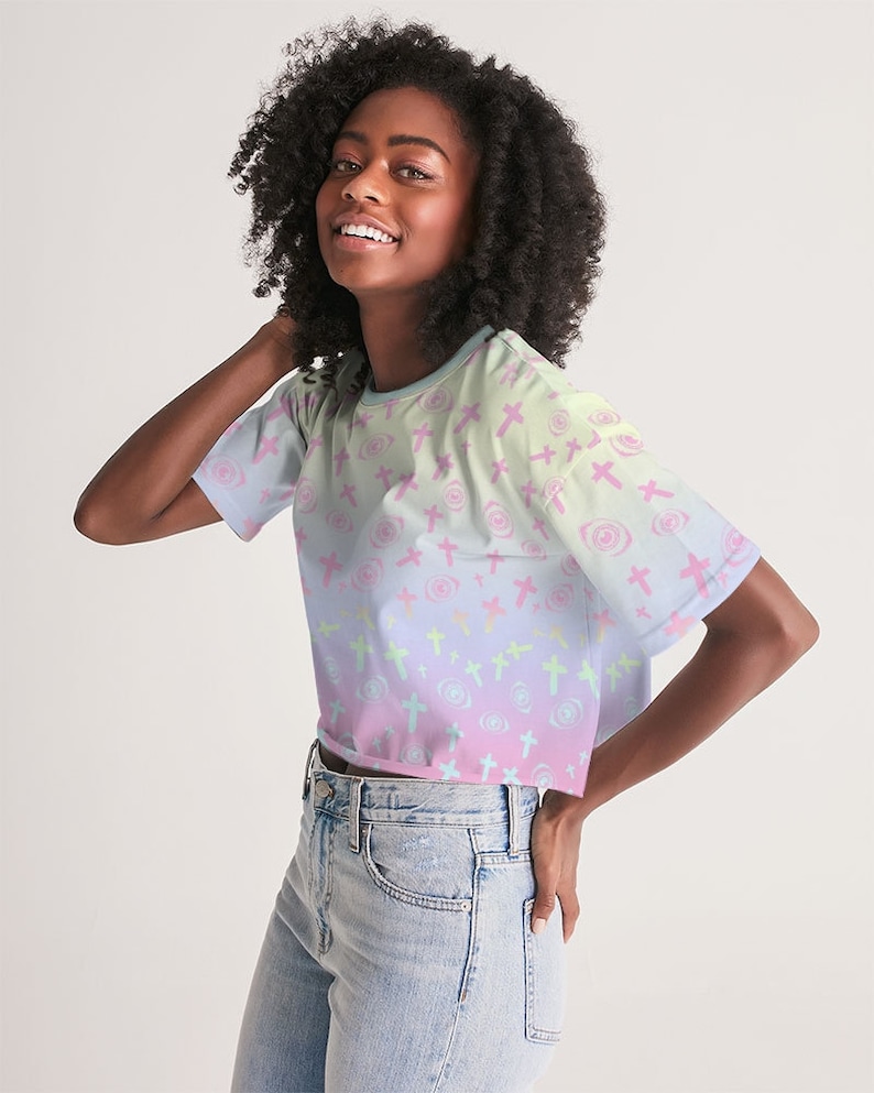 May include: A pastel pink, blue and green cropped t-shirt with a repeating pattern of crosses and swirls. The shirt has short sleeves and a relaxed fit.