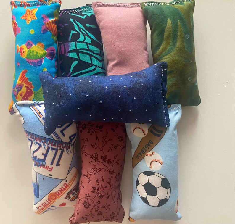 May include: A collection of nine colorful fabric pillows with various patterns and designs. The pillows are made of soft, plush fabric and are perfect for adding a touch of personality to any room.