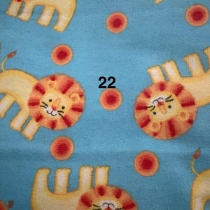 May include: A light blue fabric featuring a repeating pattern of cartoon lions and red circles. The lions are yellow with orange manes and tails. The number "22" is printed in black.