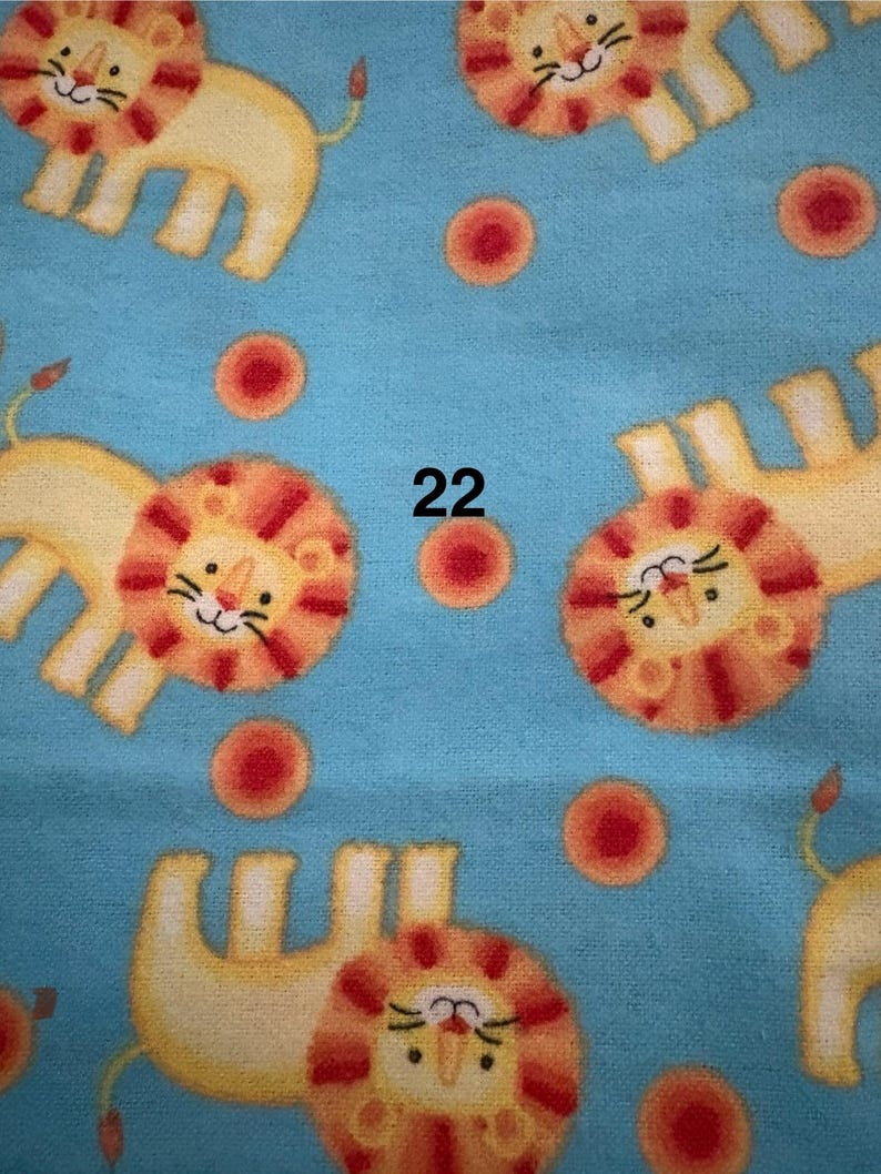 May include: A light blue fabric featuring a repeating pattern of cartoon lions and red circles. The lions are yellow with orange manes and tails. The number "22" is printed in black.