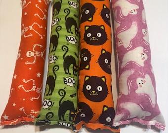 May include: Four rectangular cat toys with Halloween-themed patterns. One is orange with white skeletons, another is green with black cats and "BOO!" text, an orange one with black cat faces, and a pink one with white ghosts.