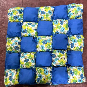 May include: A blue and white quilted throw blanket with a floral pattern. The blanket is made up of individual squares that are sewn together.