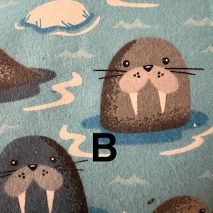 May include: A light blue fabric featuring a pattern of cartoon walruses in water. The walruses are grey with large tusks. The letter "B" is printed in black on the fabric.