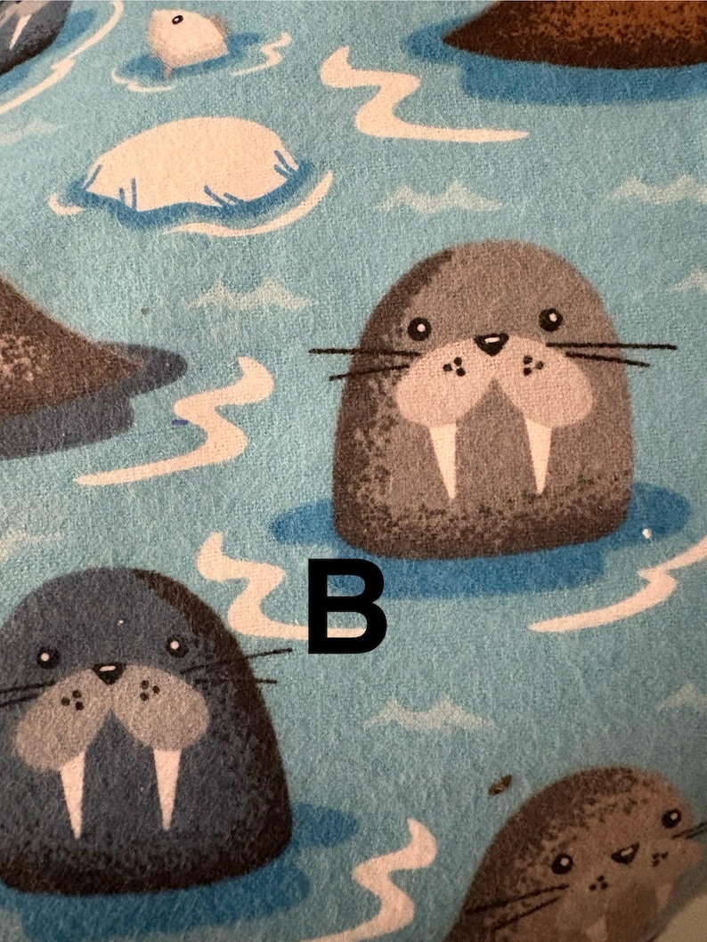 May include: A light blue fabric featuring a pattern of cartoon walruses in water. The walruses are grey with large tusks. The letter "B" is printed in black on the fabric.