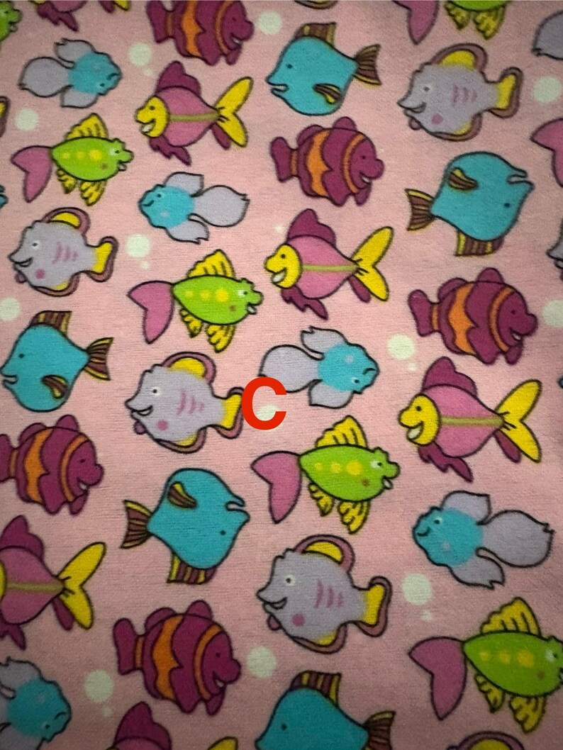 May include: A pink fabric featuring a repeating pattern of cartoon fish. The fish are in various colours, including blue, purple, green, and orange, with yellow fins and pink tails. The fish have smiling faces.