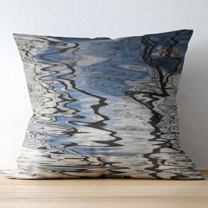 May include: A decorative throw pillow with a blue and white abstract pattern. The pattern resembles water with reflections of trees and sky.