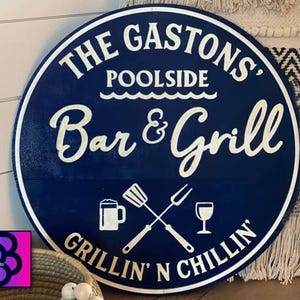 May include: A round, navy blue wooden sign with white lettering that reads "THE GASTONS' POOLSIDE Bar & Grill GRILLIN' N CHILLIN'". The sign features illustrations of a beer mug, spatula, fork, and wine glass.