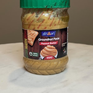 May include: A jar of Afriart Groundnut Paste Peanut Butter, 450g, with a green lid and a clear plastic wrap. The label features a peanut butter swirl illustration and the words "100% Natural."