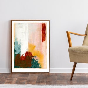 Op de afbeelding: Abstract schilderij in een bruin frame met tinten wit, roze, geel, rood en groen. Het schilderij hangt aan een witte muur boven een beige fauteuil.