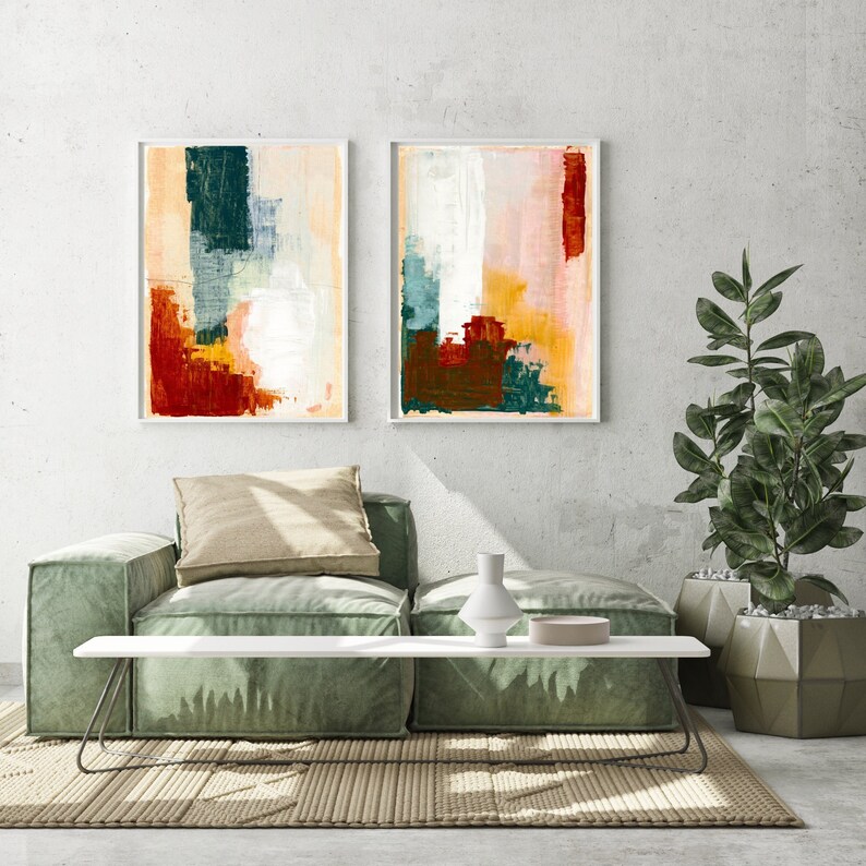 Op de afbeelding: Twee abstracte schilderijen met geometrische vormen in tinten rood, oranje, geel, groen en blauw. De schilderijen zijn wit ingelijst en hangen aan een witte muur boven een groene bank.