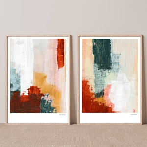 Op de afbeelding: Twee ingelijste abstracte schilderijen met een witte achtergrond en kleurrijke penseelstreken in tinten rood, oranje, geel, groen en blauw. De schilderijen zijn in houten lijsten en hebben het woord "daydream" gedrukt in de rechterbenedenhoek.