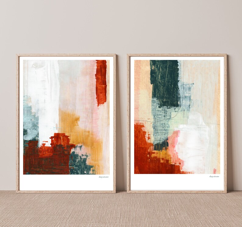Op de afbeelding: Twee ingelijste abstracte schilderijen met een witte achtergrond en kleurrijke penseelstreken in tinten rood, oranje, geel, groen en blauw. De schilderijen zijn in houten lijsten en hebben het woord "daydream" gedrukt in de rechterbenedenhoek.