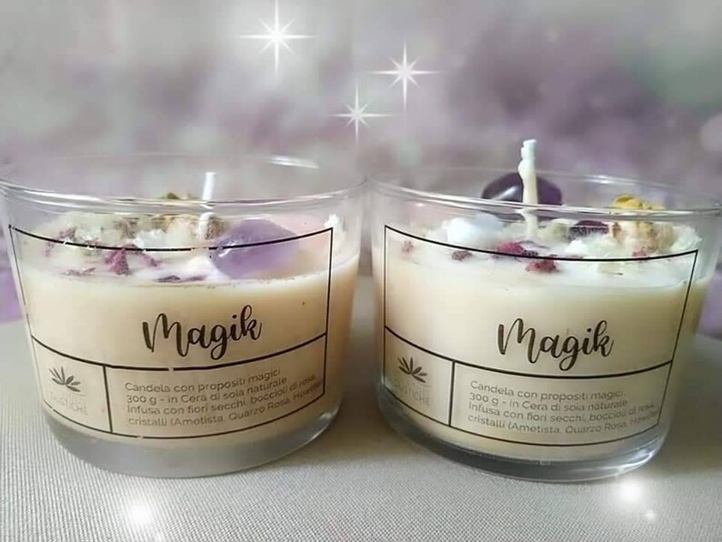 May include: Two glass jars with a white candle and crystals inside. The jars have labels that say "Magik" and include the text "Candela con propositi magici 300g - in Cera di soia naturale Infusa con fiori secchi, boccioli di rosa, cristalli (Ametista, Quarzo Rosa, Howlite)"