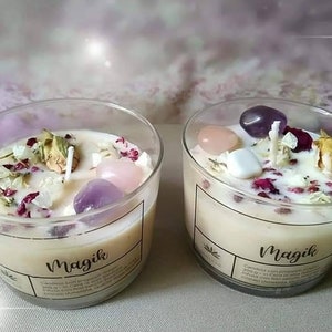 May include: Two glass candle jars with white candles and crystals inside. The jars are labeled "Magik" and have a floral design.