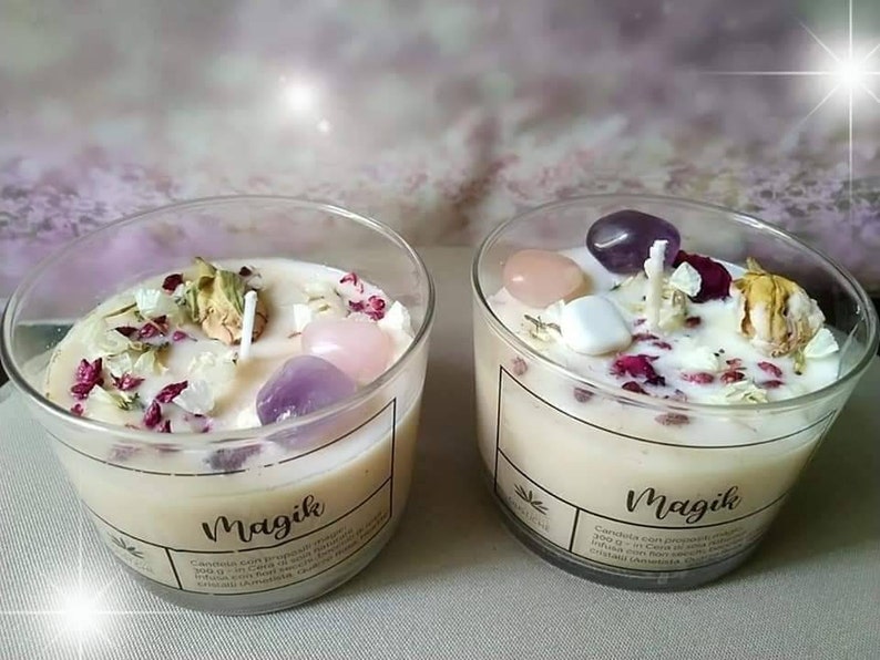 May include: Two glass candle jars with white candles and crystals inside. The jars are labeled "Magik" and have a floral design.