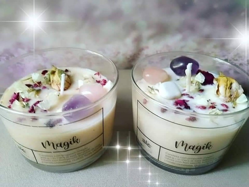 May include: Two clear glass candle jars with white wax and embedded crystals, dried flowers, and a wick. The jars have a black label with the word "Magik" printed on them.