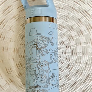 May include: A light blue Yeti water bottle with a stainless steel body and a black and white outline of Toy Story characters on the side. The bottle has a black handle and the word "YETI" is printed on the top.