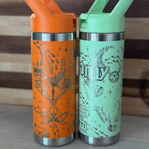 May include: Two stainless steel water bottles with a Harry Potter theme. The bottle on the left is orange with gold accents and the bottle on the right is green with silver accents. Both bottles have a design of the Hogwarts Express, the Golden Snitch, and the Deathly Hallows symbol.