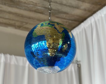 May include: A blue and gold disco ball with a world map design hangs from a silver chain against a white background.