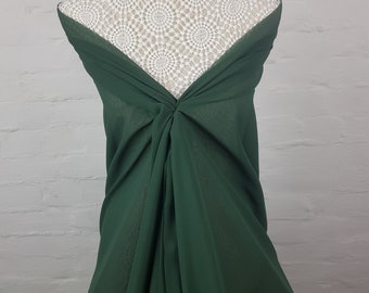 May include: A dark green fabric draped over a mannequin. The fabric is gathered and twisted at the center, creating a flowing, elegant look. The background is a white brick wall.