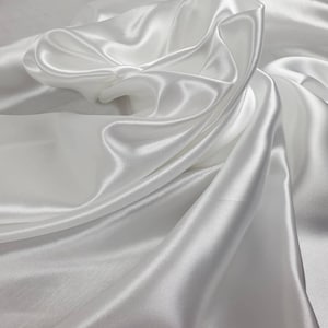 May include: White satin fabric with soft, flowing folds and a smooth, luxurious texture.
