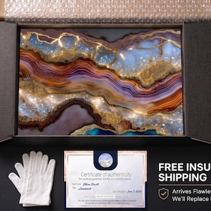 May include: A rectangular wall art piece featuring a swirling agate-inspired design with layers of deep purple, burnt orange, and blue, accented by shimmering gold veins and crystalline textures, presented in a black shipping box with a certificate.