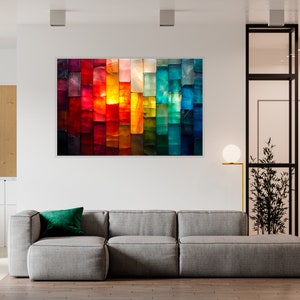 May include: An abstract artwork featuring a vibrant spectrum of colours, from deep reds to cool blues. The artwork is mounted above a grey sectional sofa with a green cushion, creating a modern living room setting.