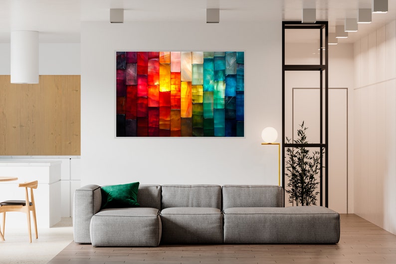 May include: An abstract artwork featuring a vibrant spectrum of colours, from deep reds to cool blues. The artwork is mounted above a grey sectional sofa with a green cushion, creating a modern living room setting.