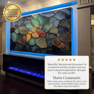 May include: A large rectangular wall art piece featuring a mosaic of irregular, multi-colored glass-like shapes in shades of teal, amber, gold, and dark grey, illuminated by blue LED backlighting above a black fireplace with blue flames.