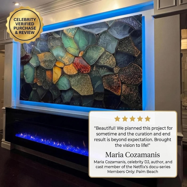 May include: A large rectangular wall art piece featuring a mosaic of irregular, multi-colored glass-like shapes in shades of teal, amber, gold, and dark grey, illuminated by blue LED backlighting above a black fireplace with blue flames.