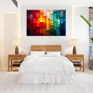 May include: A bedroom with a bed dressed in white bedding and a wooden headboard. Two wooden bedside tables with lamps stand on either side of the bed. Above the bed is a colourful abstract painting with red, orange, yellow, green, and blue tones.