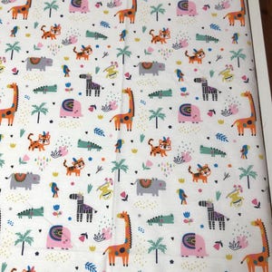 May include: White fitted crib sheet with a colorful safari animal print. The pattern includes giraffes, tigers, zebras, hippos, crocodiles, birds, and palm trees. The animals are in orange, pink, green, and purple.