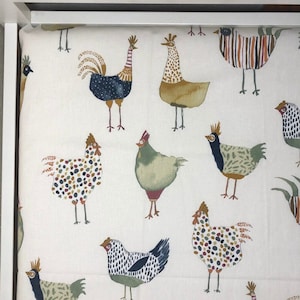 May include: A white fabric with a repeating pattern of colorful chickens. The chickens are illustrated in a whimsical style with various colors and patterns.