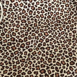 May include: A close-up of a fabric with a brown and tan leopard print pattern.