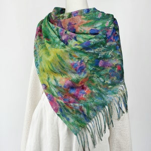 May include: A colorful scarf with a floral design in shades of green, blue, pink, and yellow. The scarf has a fringed edge and is draped over a white sweater and dress form.