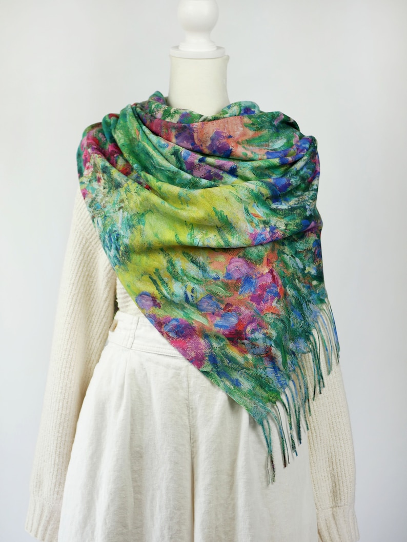 May include: A colorful scarf with a floral design in shades of green, blue, pink, and yellow. The scarf is draped over a mannequin and has a fringed edge. The scarf appears to be made of a soft, lightweight material.