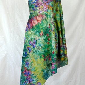 May include: A one-shoulder garment draped over a mannequin, showcasing a vibrant floral print. The fabric features a lush garden scene with green, yellow, pink, and purple hues, reminiscent of an impressionist painting. The garment is likely a scarf or shawl.