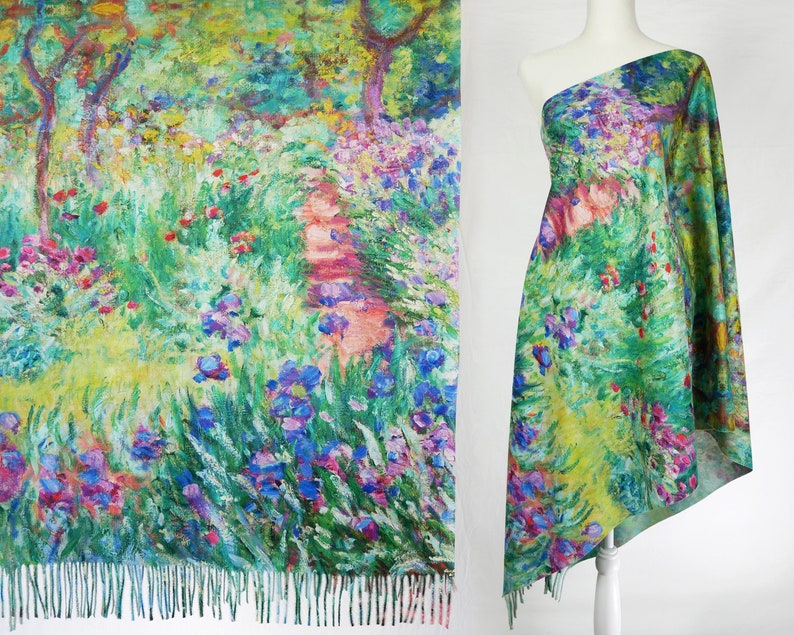 May include: A shawl featuring a vibrant impressionist garden scene with irises, trees, and a path. The fabric is draped over a mannequin, showcasing the design's colors of green, blue, pink, and yellow. The shawl has a fringed edge.