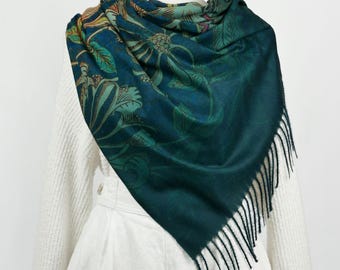 May include: A teal blue scarf with a floral pattern and fringe. The scarf is draped over a white sweater and white pants.