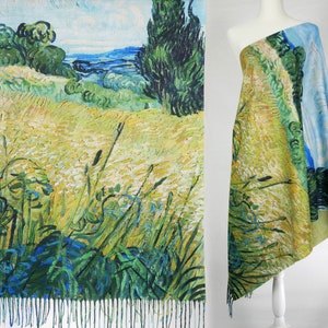 May include: A woven shawl featuring a colourful print of a landscape painting. The painting depicts a field of wheat, a blue sky, and a green tree. The shawl has a fringed edge.