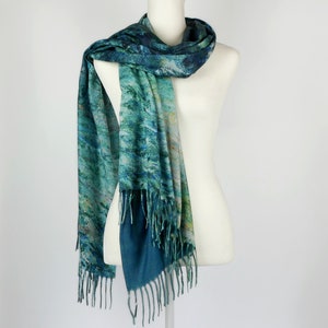 K&ouml;nnte beinhalten: Ein t&uuml;rkis-blauer Schal mit aquarellartigem Design ist &uuml;ber eine wei&szlig;e Schaufensterpuppe drapiert. Der Schal hat einen Fransenrand und einen dunkelblauen Rand. Das Muster des Schals umfasst T&uuml;rkis-, Blau- und Gelbt&ouml;ne.