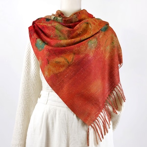 May include: A red scarf with a colourful abstract print and fringe edges. The scarf is draped over a white mannequin.