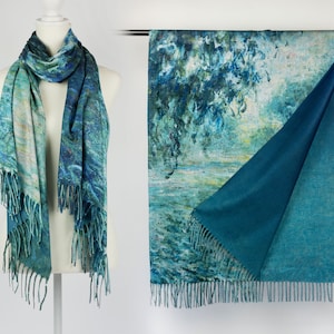 K&ouml;nnte beinhalten: Wendescharf mit einem blau-gr&uuml;nen impressionistischen Gem&auml;ldedesign. Eine Seite zeigt eine detaillierte Landschaft, w&auml;hrend die andere einfarbig t&uuml;rkis ist. Der Schal hat einen Fransenrand und wird auf einer Schaufenquin und einer Kleiderstange pr&auml;sentiert.