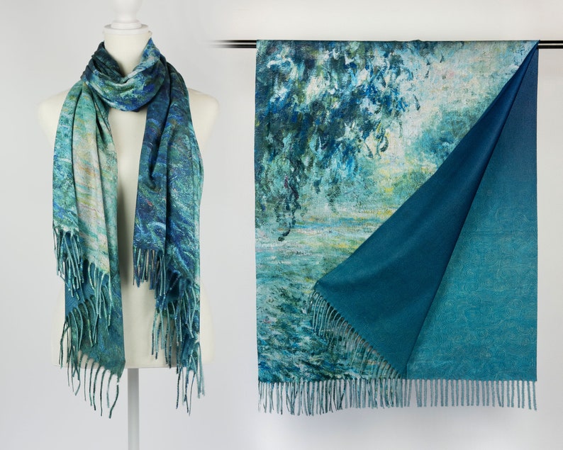 K&ouml;nnte beinhalten: Wendescharf mit einem blau-gr&uuml;nen impressionistischen Gem&auml;ldedesign. Eine Seite zeigt eine detaillierte Landschaft, w&auml;hrend die andere einfarbig t&uuml;rkis ist. Der Schal hat einen Fransenrand und wird auf einer Schaufenquin und einer Kleiderstange pr&auml;sentiert.