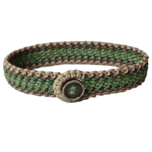 Può includere: Braccialetto fatto a mano con un design intrecciato nei toni del verde, marrone e beige. Il braccialetto è assicurato con un grande bottone rotondo. Il motivo intrecciato crea un aspetto strutturato, e i colori neutri lo rendono versatile.